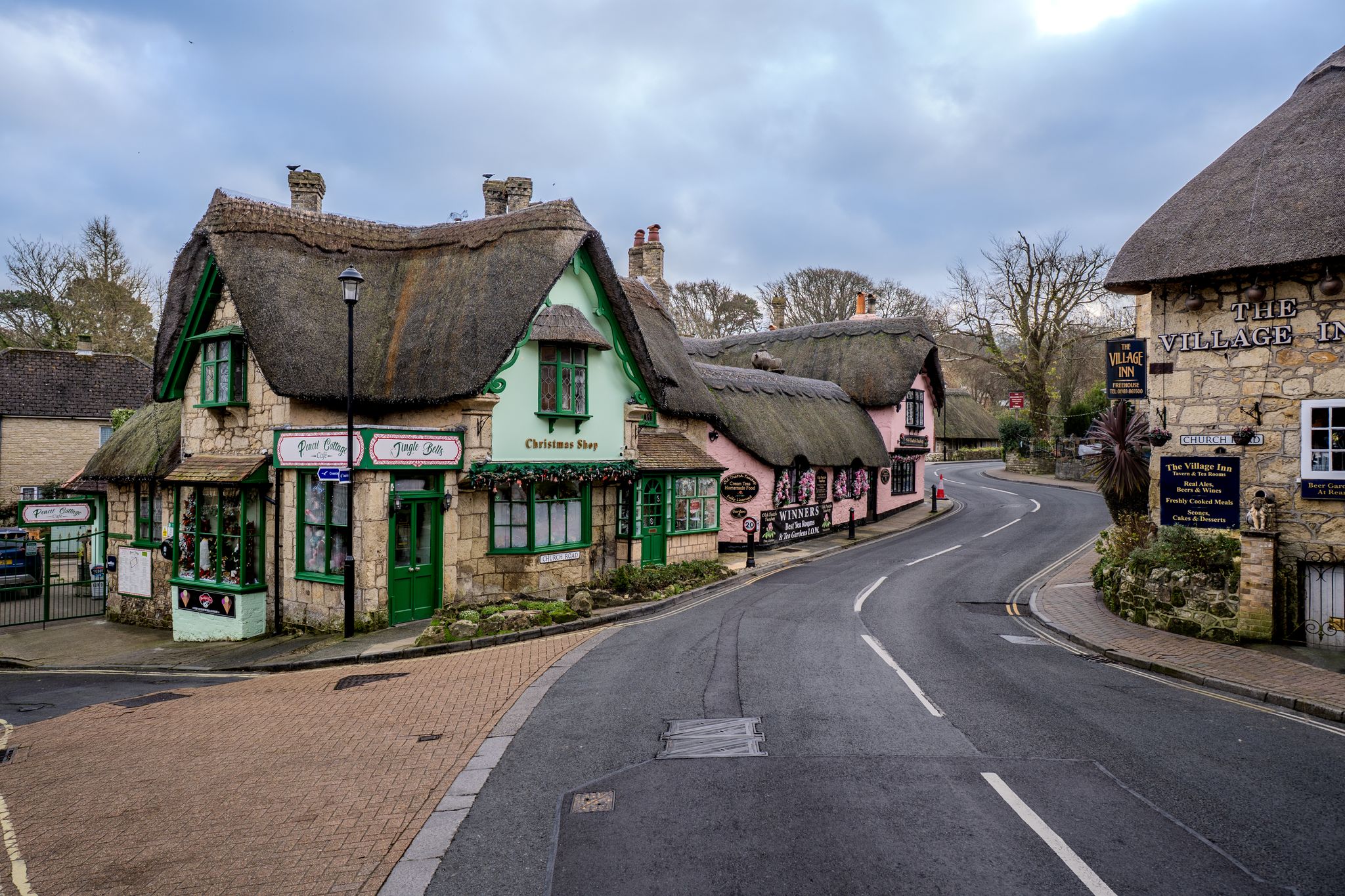 Picturesque street in an English village with traditional thatched roof buildings and shops.